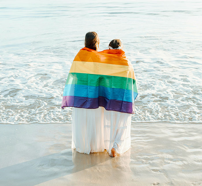 Two women standing on the beach wrapped in a rainbow flag symbolizing family ties and old fight with stepsister. Two women standing on the beach wrapped in a rainbow flag symbolizing family ties and old fight with stepsister.