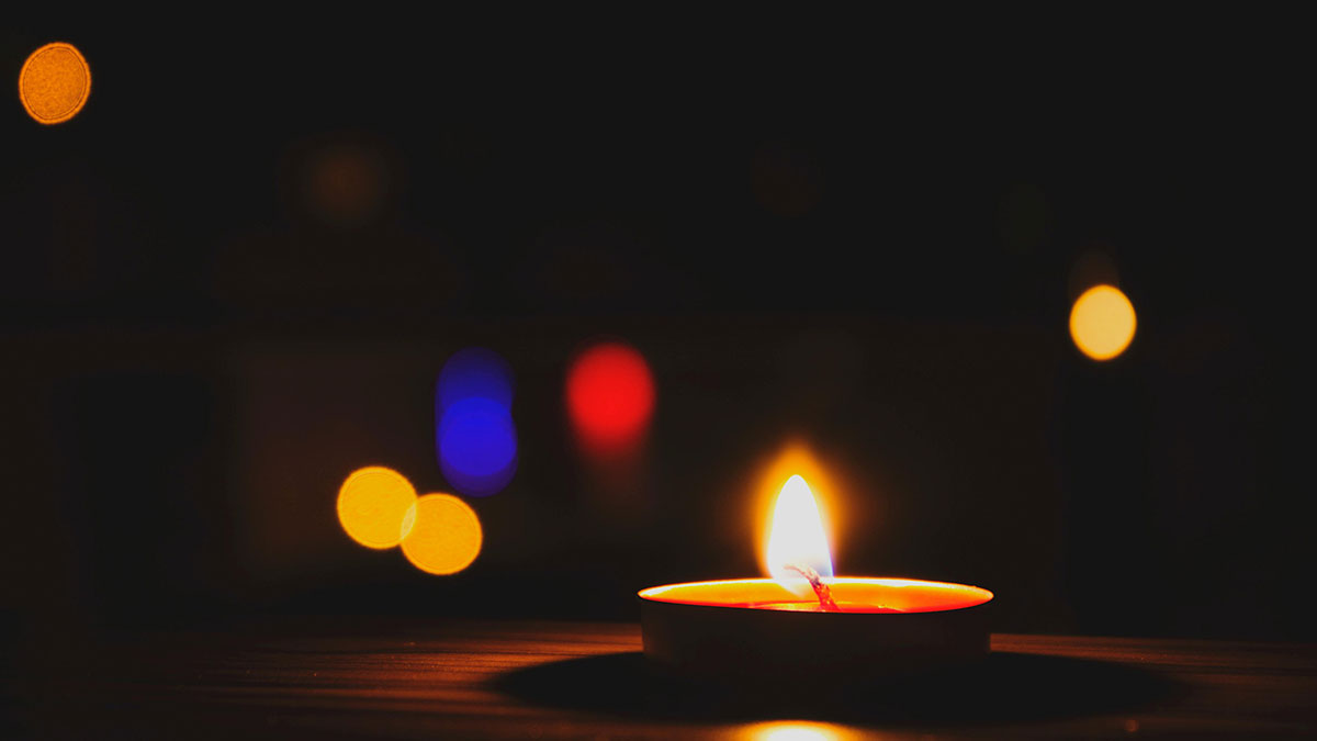 Candle flame glowing in the dark with blurred colorful lights, symbolizing tiny human mistakes in history.