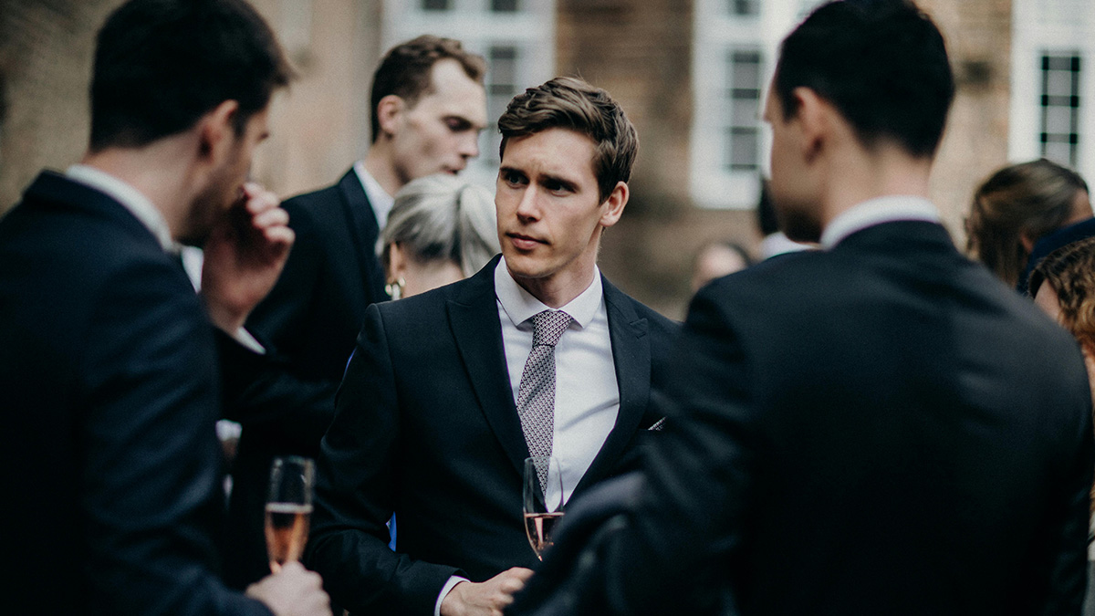 Group of young professionals using social cheat codes at a formal outdoor networking event, dressed in suits.