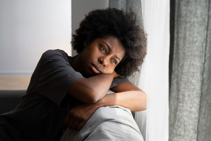 Teen boy upset after mom suggests his black girlfriend dress more comfortably, sitting by window in thoughtful mood. Teen boy upset after mom suggests his black girlfriend dress more comfortably, sitting by window in thoughtful mood.