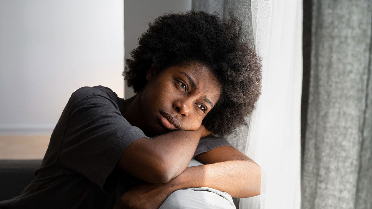 Thoughtful Black teenager resting head on arms looking out window, reflecting on a difficult conversation about dress code.