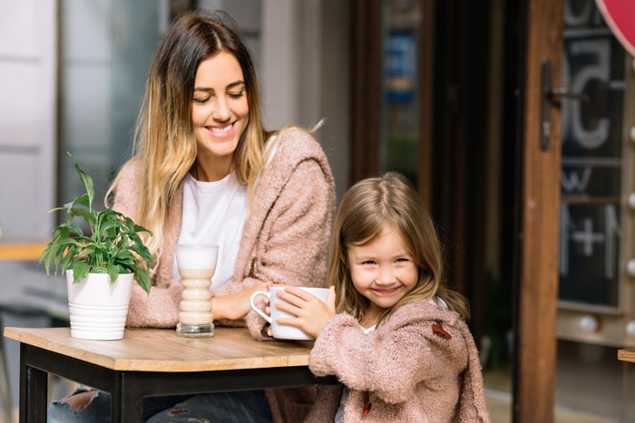 Woman on a 12-month hiatus from work smiling with child at café table, expecting more money than £150 weekly allowance. Woman on a 12-month hiatus from work smiling with child at café table, expecting more money than £150 weekly allowance.