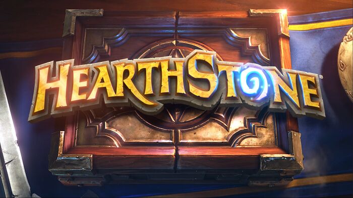 Hearthstone digital card game logo with wooden texture and glowing blue swirl on a fantasy-themed background.