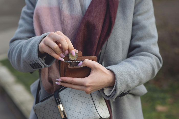 Woman holding wallet outdoors, putting a coin inside while wearing a gray coat and scarf, illustrating karma at grocery store.