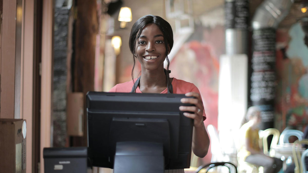 Smiling cashier standing behind register at grocery store counter helping customers with checkout process