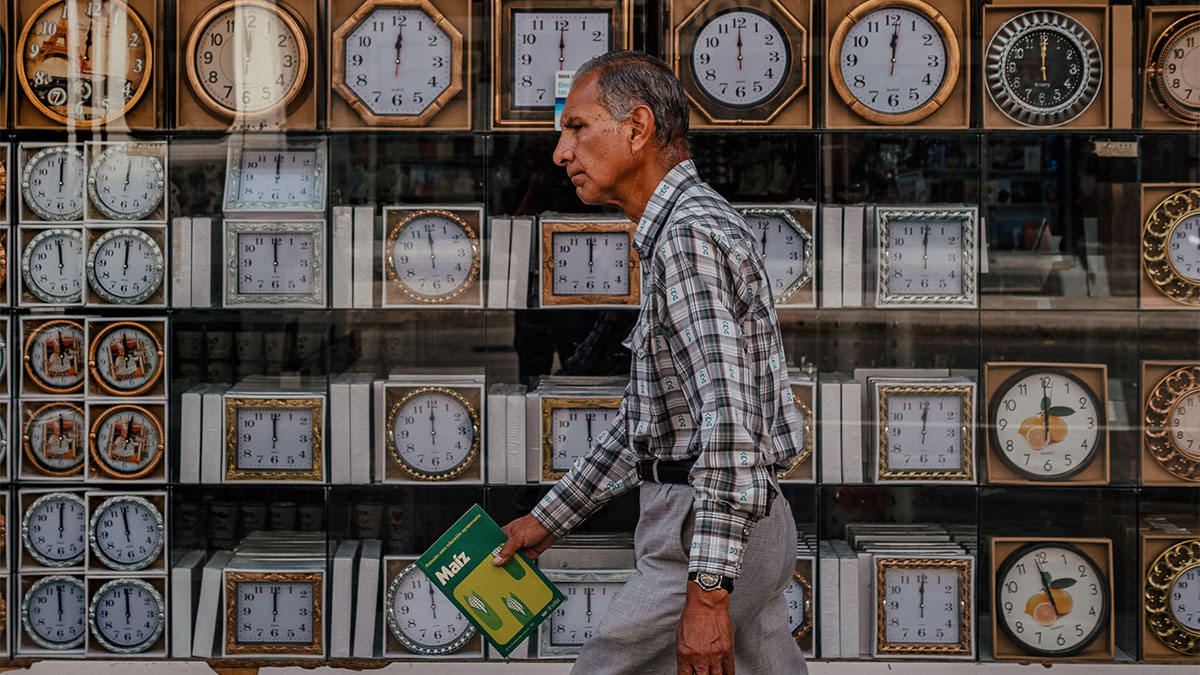 Man walking past a shop window filled with various clocks, captured in a street photography shot.