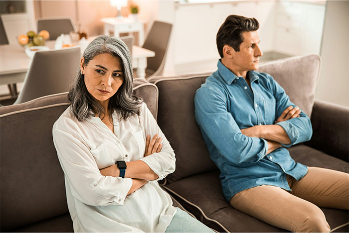 Wife and husband sitting on couch with arms crossed, showing tension and resentment during a serious moment. Wife and husband sitting on couch with arms crossed, showing tension and resentment during a serious moment.