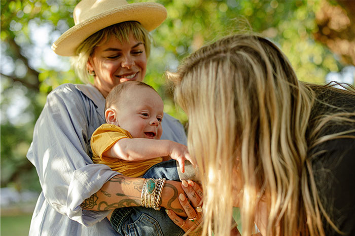 Mother holding baby outdoors while another woman interacts, capturing moments of family and connection on a reluctant trip. Mother holding baby outdoors while another woman interacts, capturing moments of family and connection on a reluctant trip.