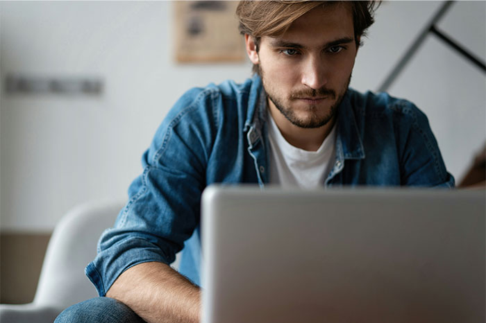Man looking upset and focused on a laptop, reflecting emotions of resentment and humiliation in a tense moment. Man looking upset and focused on a laptop, reflecting emotions of resentment and humiliation in a tense moment.