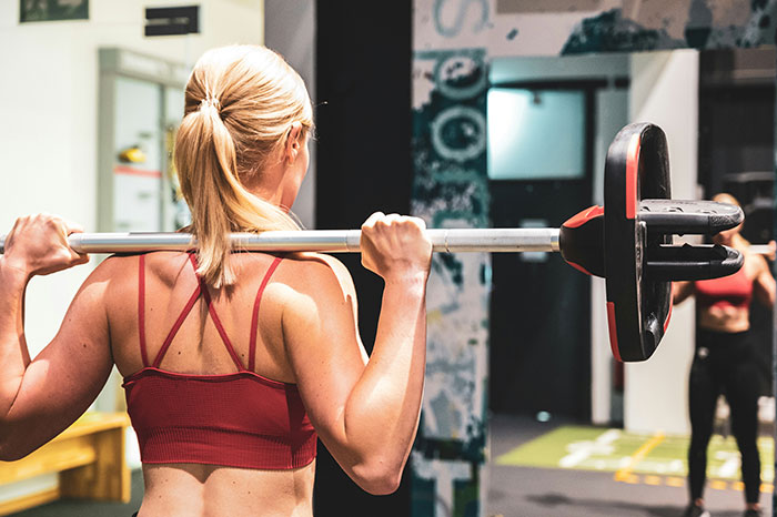 Woman lifting barbell in gym, showing toned back and arms, focused on strength training workout session. Woman lifting barbell in gym, showing toned back and arms, focused on strength training workout session.