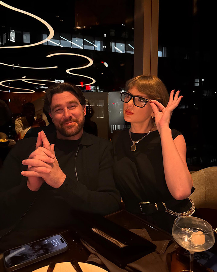 Travis Kelce and Taylor Swift seated at a table in a dimly lit restaurant with modern ceiling lights. Travis Kelce and Taylor Swift seated at a table in a dimly lit restaurant with modern ceiling lights.