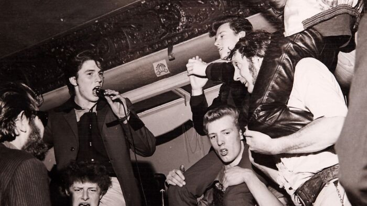 Young men in vintage 20th century teddy boy era style gathered at a lively social event, dressed in classic attire.