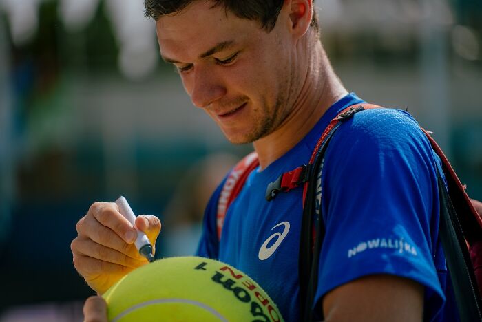 Polish CEO signing a large tennis ball outdoors, associated with US Open hat snatcher story. Polish CEO signing a large tennis ball outdoors, associated with US Open hat snatcher story.