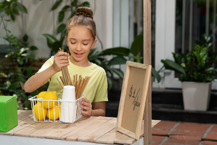 Young girl playing with straws and lemons at a lemonade stand, evoking childhood memories that felt sweet back then.