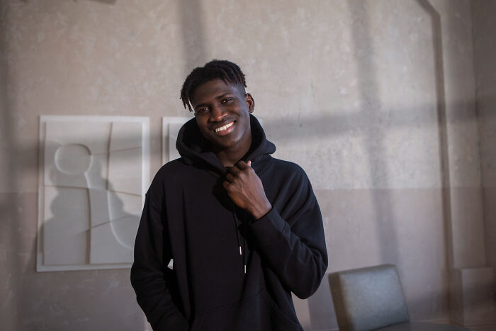 Young man smiling indoors wearing a black hoodie, evoking childhood memories that felt sweet but became unsettling in retrospect.