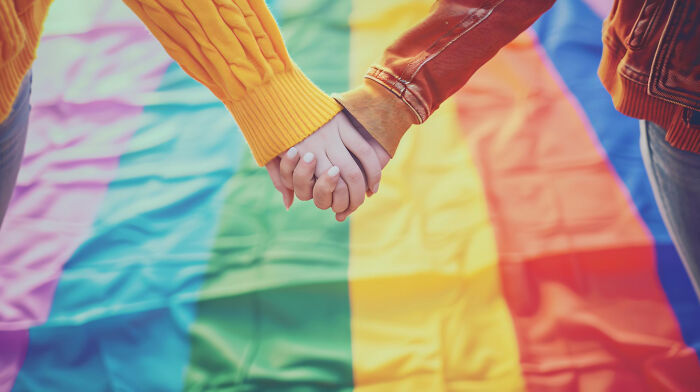 Two people holding hands over a colorful rainbow flag illustrating childhood memories that felt sweet but became unsettling