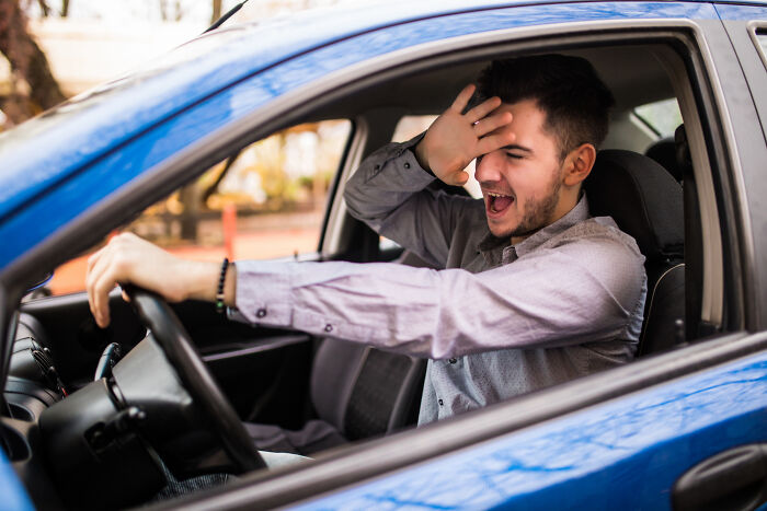 Young man in a blue car smiling and shielding his eyes, evoking childhood memories that felt sweet but became unsettling in retrospect