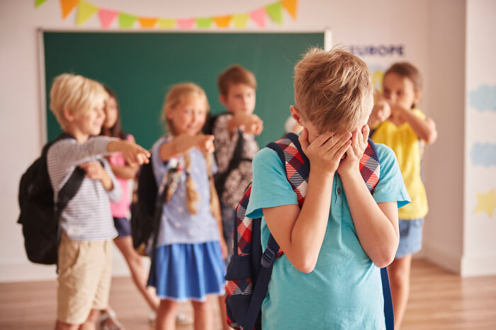 Group of school children pointing and laughing at a boy covering his face, reflecting childhood memories that felt sweet but unsettling.