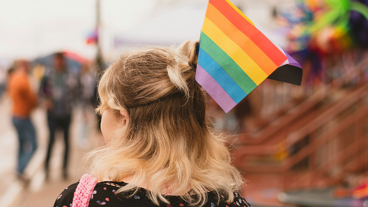 Person with rainbow pride flag in hair at a busy outdoor event, highlighting things mentioned after marriage discussions.