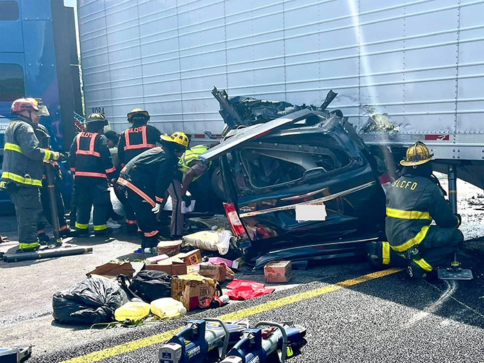 Firefighters attending to a crushed car after a truck driver made an illegal U-turn causing a fatal accident with three deaths. Firefighters attending to a crushed car after a truck driver made an illegal U-turn causing a fatal accident with three deaths.