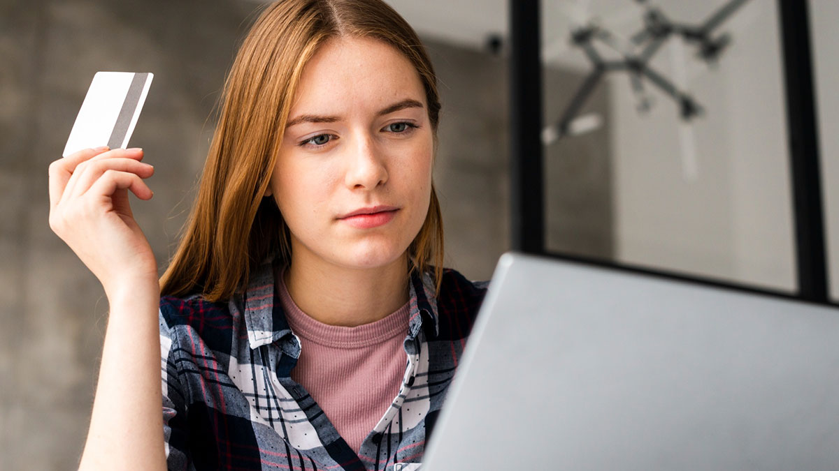 Young woman holding a credit card and looking at a laptop screen, with global disasters risk concept in mind.