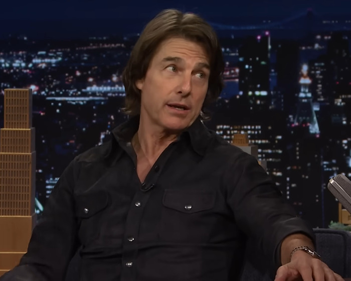 Tom Cruise speaking in a late-night talk show setting with a city skyline backdrop at night. Tom Cruise speaking in a late-night talk show setting with a city skyline backdrop at night.