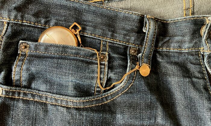 Close-up of a vintage pocket watch in the small pocket of blue denim jeans highlighting gender-based double standards.