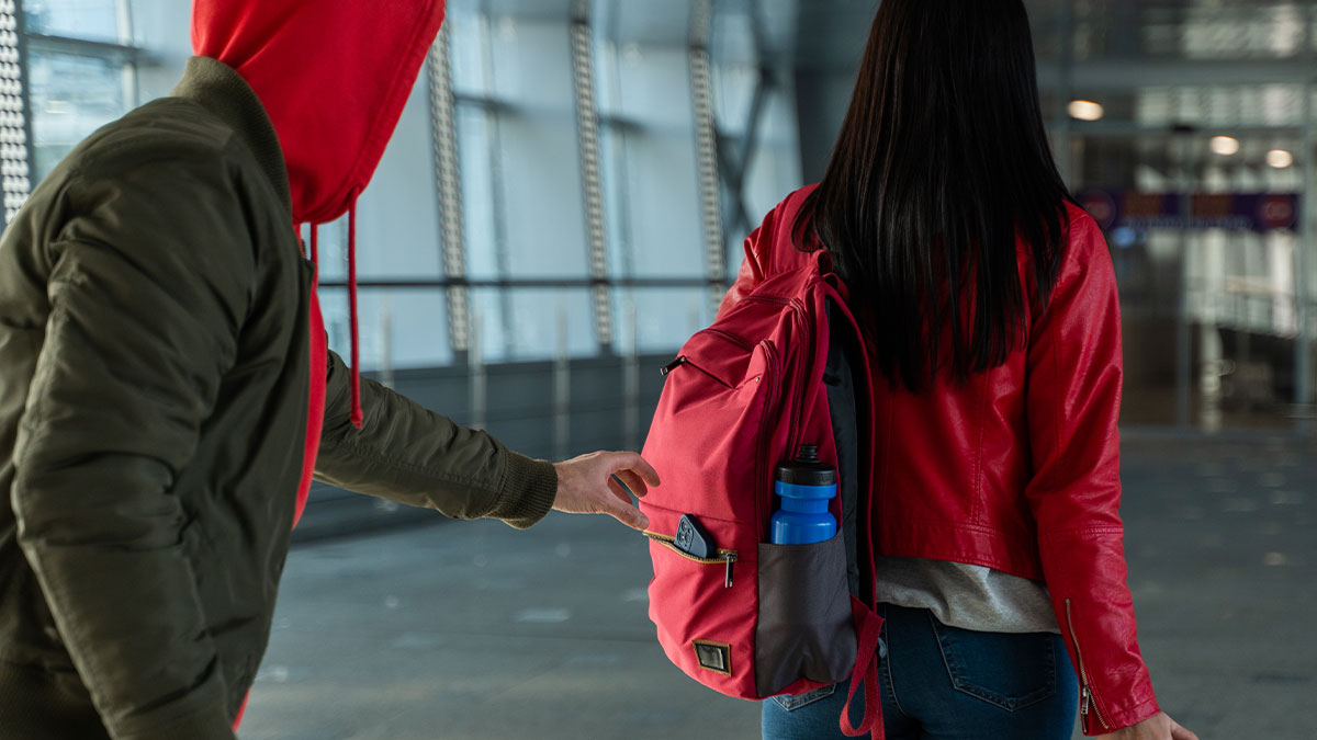 Person in red hoodie attempting to pickpocket a tourist wearing a red jacket and backpack in a public area.