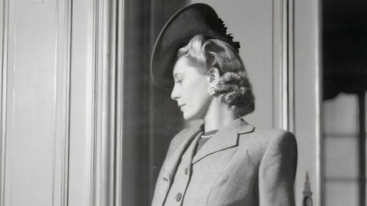 Elegant British woman in WWII fashion wearing a tailored suit and stylish hat, showcasing style during wartime restrictions.