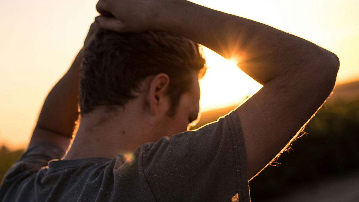 Man with hands behind head at sunset, reflecting on being fine with being alone and unattractive feelings