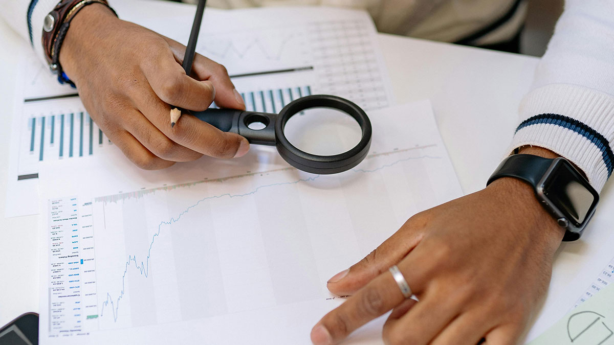 Person analyzing financial charts with a magnifying glass and pencil, symbolizing jobs without a soul concept.