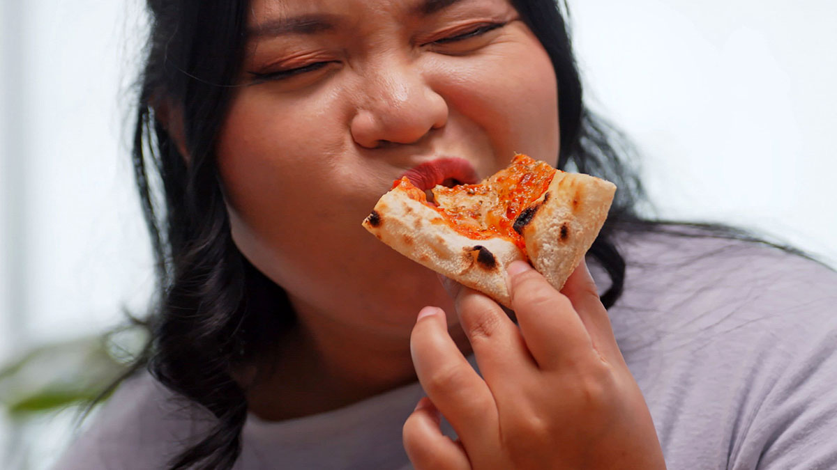 Person eating pizza slice, illustrating challenges faced by individuals working to lose weight successfully.