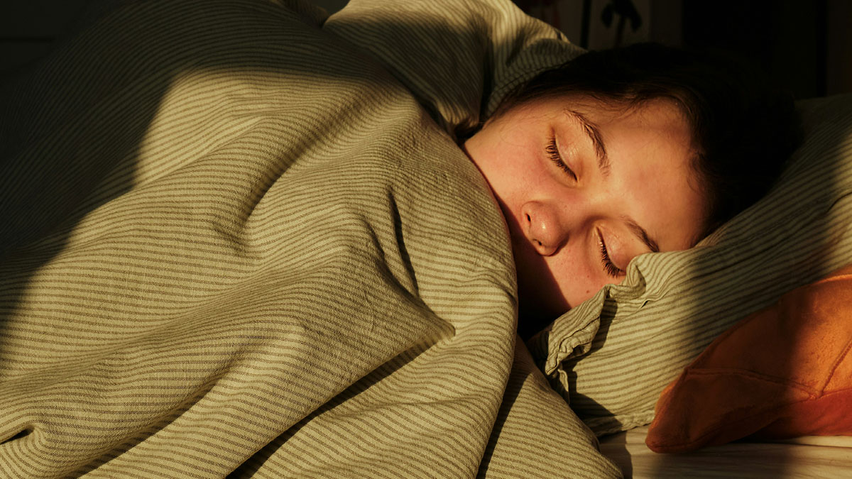 Person asleep under striped blanket with sunlight casting shadows, evoking a spooky and terrifying encounter atmosphere.
