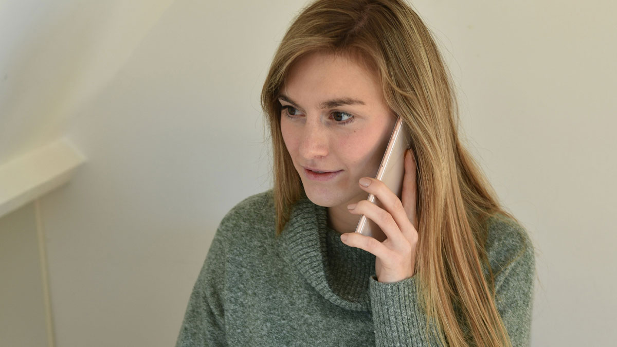 Young woman in a green sweater talking on the phone, illustrating unusual reasons people shared for missing work humorously