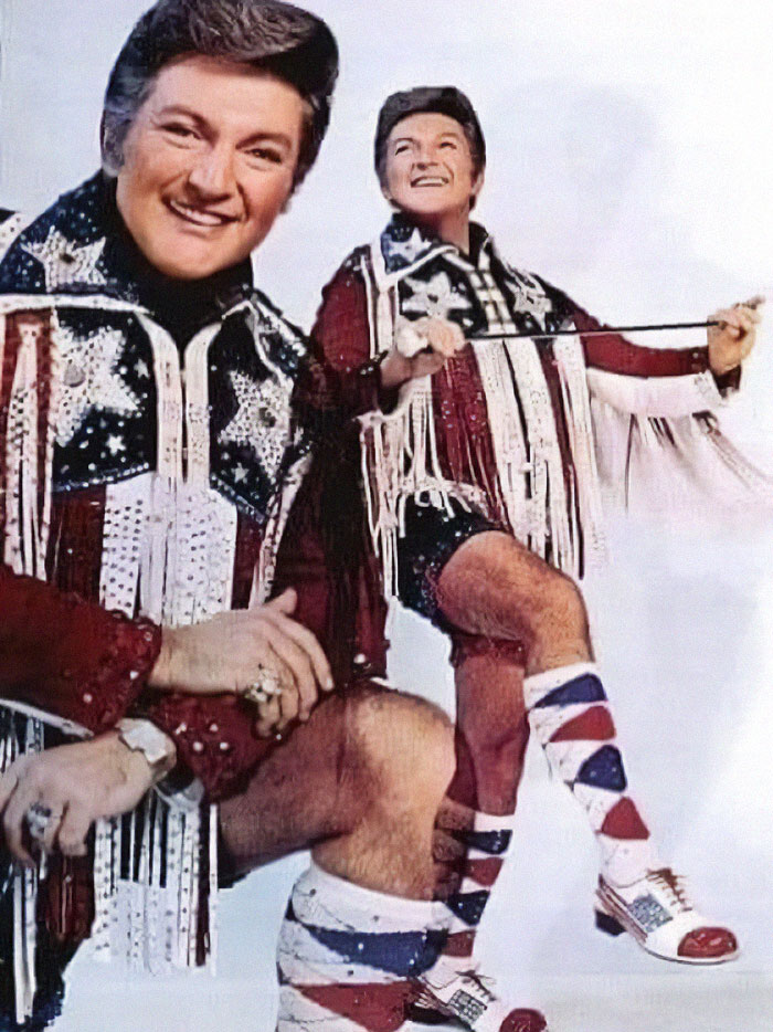 Man in vintage star-spangled outfit and fringed jacket, posing playfully in a nostalgic old-timey style photo.