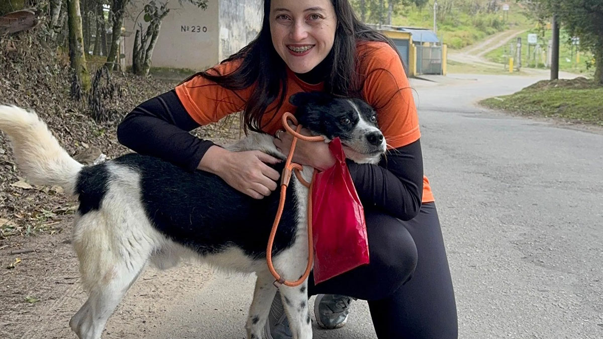 Woman kneeling and smiling while hugging a happy shelter dog on their weekly walk outdoors along a paved road.