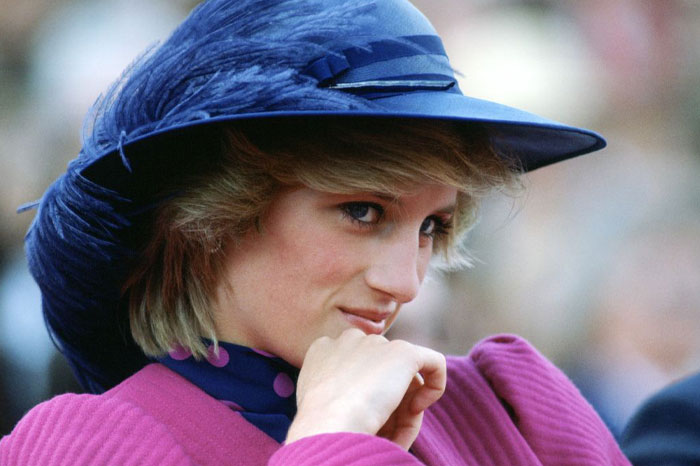 Woman wearing a blue feathered hat and pink outfit, showing a thoughtful expression related to water sign traits.