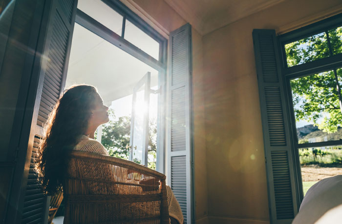 Woman with long curly hair sitting in a chair near open door, reflecting and enjoying sunlight, representing water sign traits.