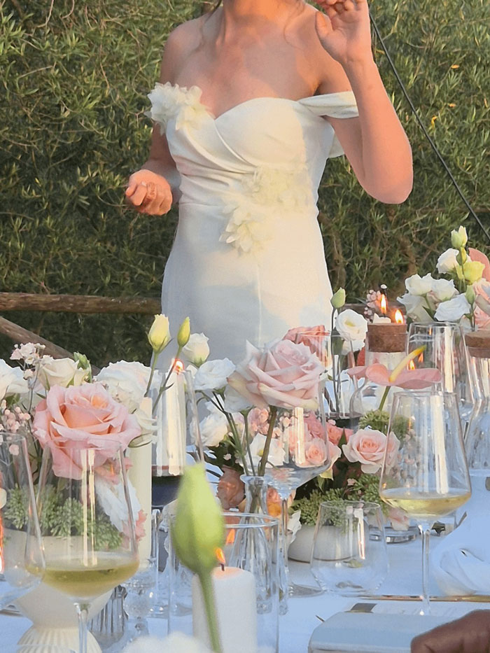 Woman wearing white wedding dress at outdoor wedding table decorated with pink roses and lit candles. Woman wearing white wedding dress at outdoor wedding table decorated with pink roses and lit candles.