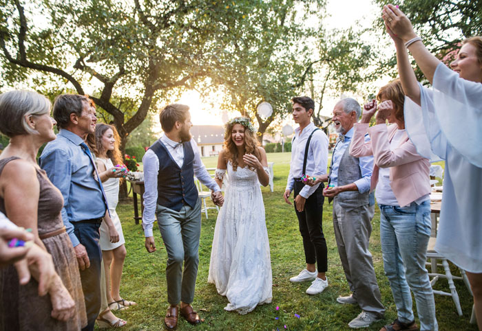 Guests celebrate a bride and groom outdoors as the groom's brother's girlfriend wears a sage green dress at the wedding ceremony. Guests celebrate a bride and groom outdoors as the groom's brother's girlfriend wears a sage green dress at the wedding ceremony.