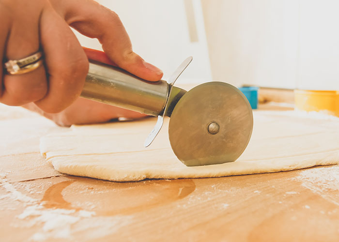 Hand using a pizza cutter on dough, illustrating one of the 93 things people assumed everyone did in their family.