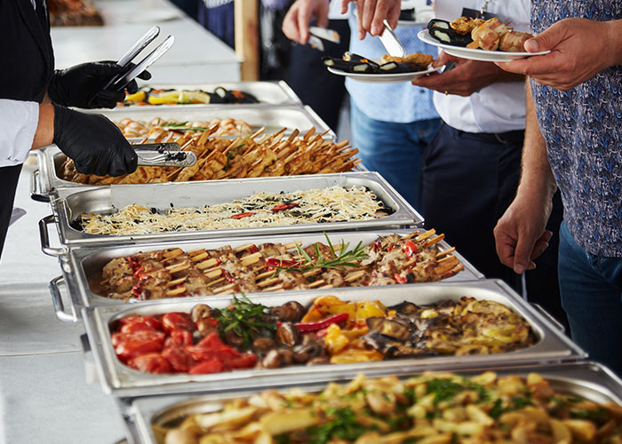 People serving themselves from a buffet with various hot dishes, illustrating family food traditions assumed by everyone.
