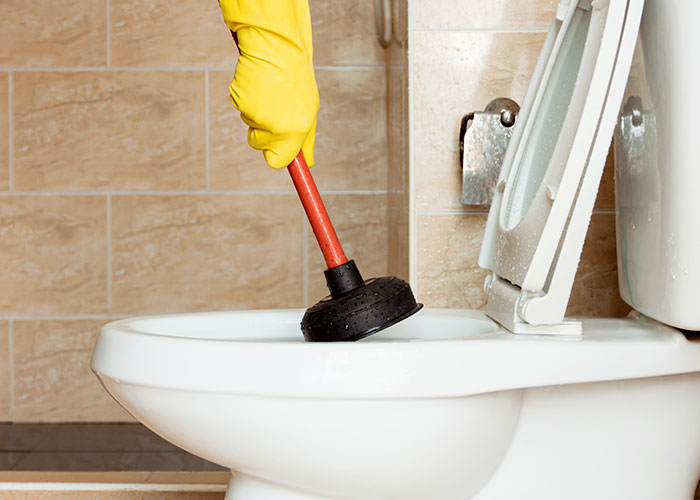 Hand in yellow glove using plunger on white toilet bowl representing family assumed chores and tasks.