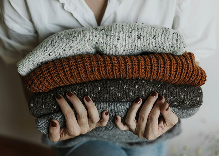 Hands holding a stack of folded sweaters, illustrating things people assumed everyone did in their family.