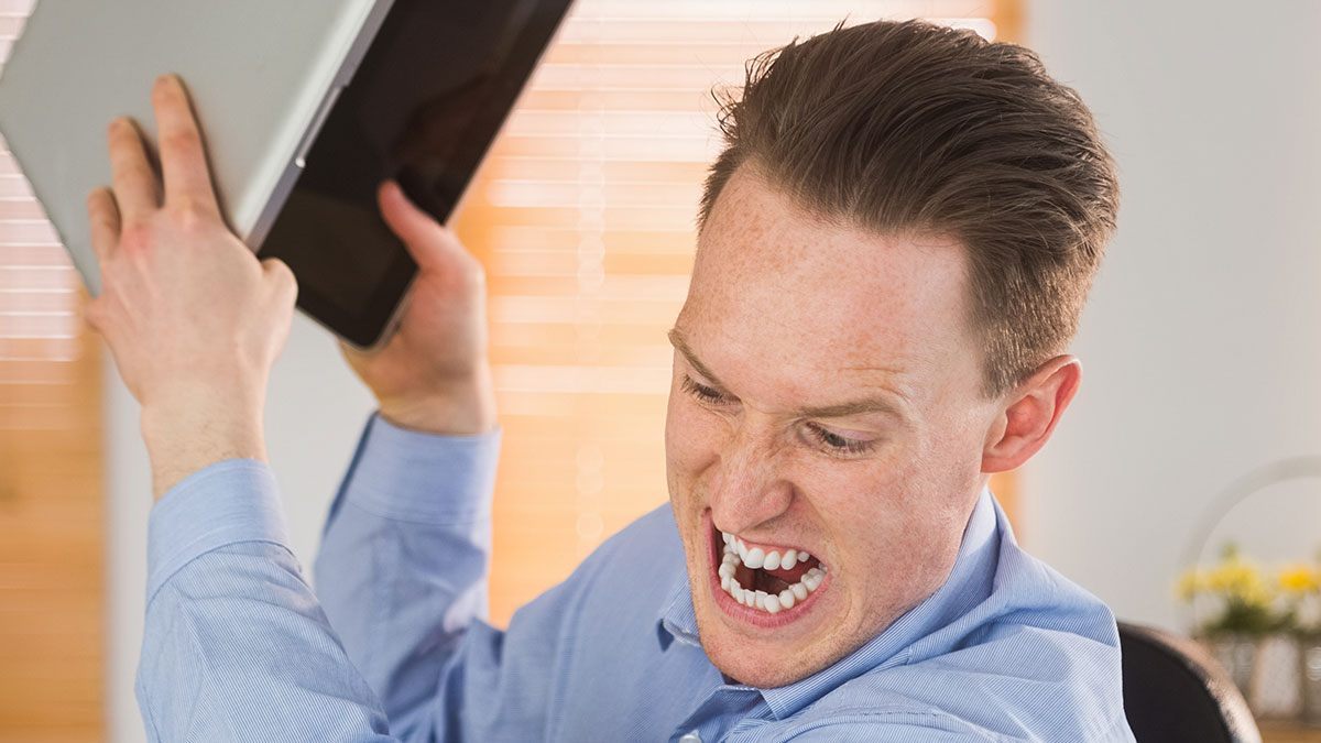 Man in blue shirt angrily raising a laptop in frustration during weird unhinged workplace incidents at office