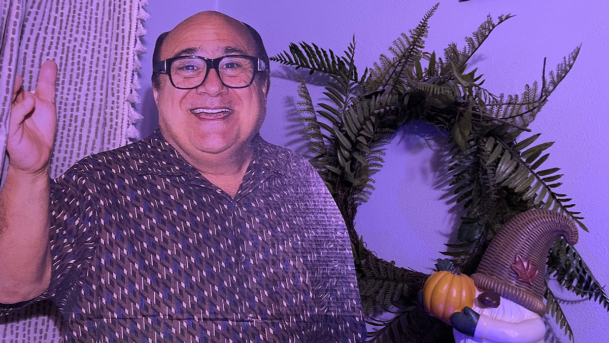 Cardboard cutout of a man smiling next to a wreath and a gnome holding a pumpkin under purple lighting.