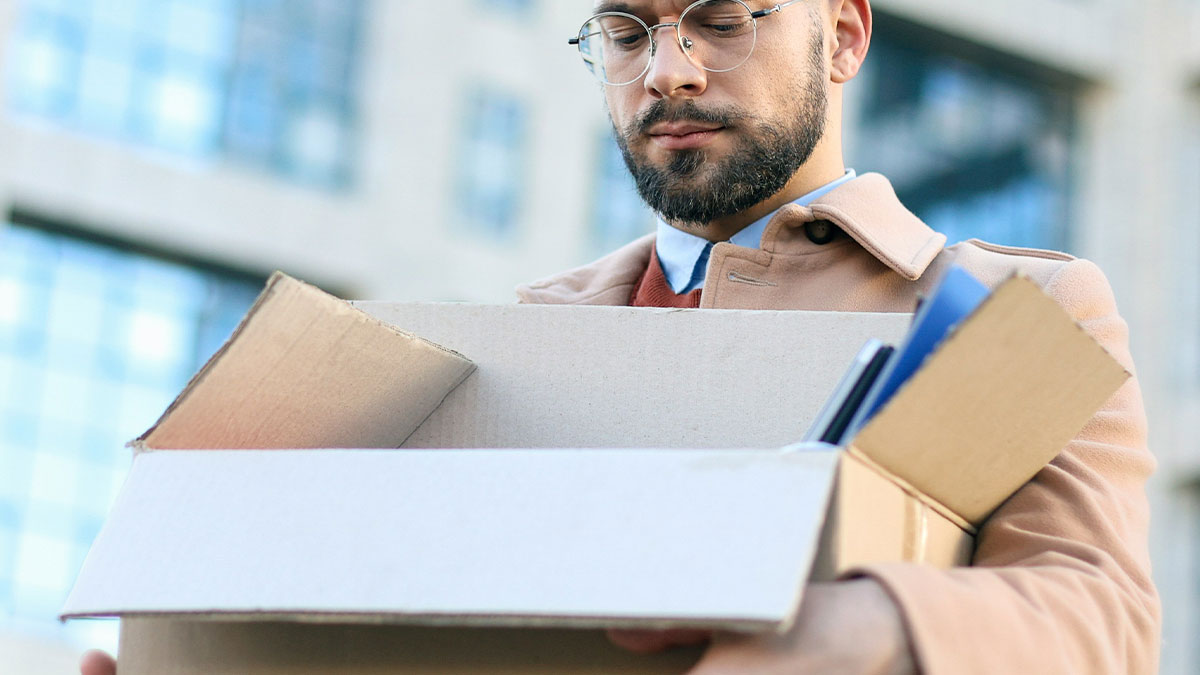 Man holding a box of personal items outside an office building, facing discipline for inappropriate work comments.