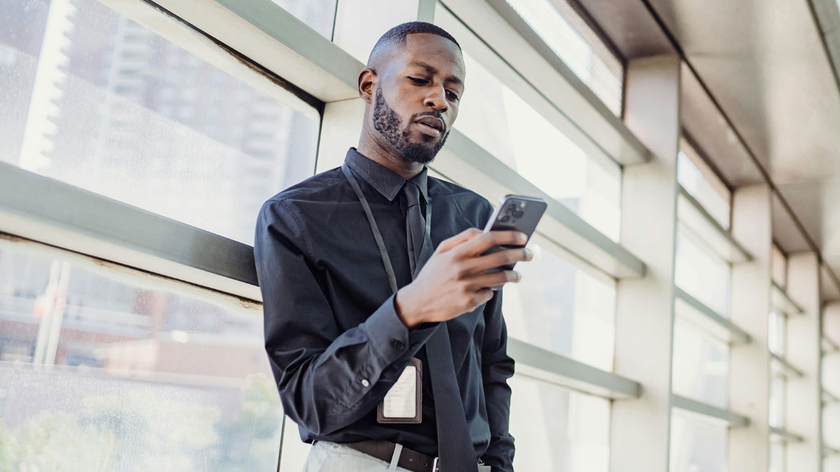 Man in black shirt and tie texting on smartphone in office hallway, wife finds husband texting coworker early in marriage.