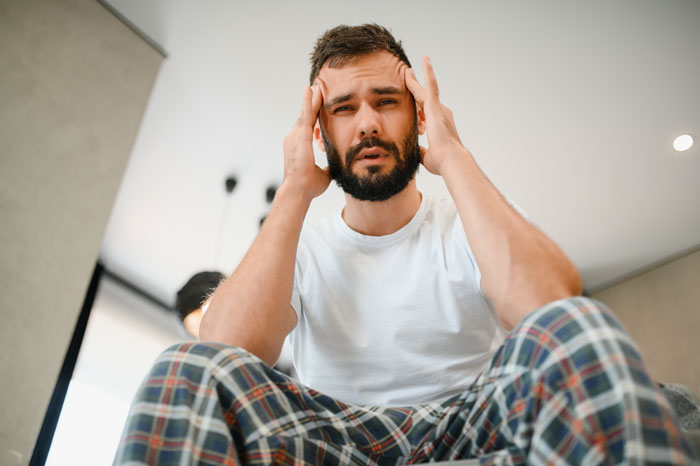 Man in pajamas holding head in frustration, representing conflict over SAHM for teens and doing no chores debate. Man in pajamas holding head in frustration, representing conflict over SAHM for teens and doing no chores debate.