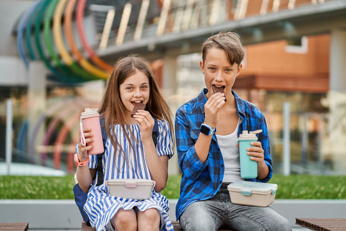 Two teens eating chocolate and holding drinks outdoors, illustrating the concept of being SAHM for teens and household chores debate. Two teens eating chocolate and holding drinks outdoors, illustrating the concept of being SAHM for teens and household chores debate.